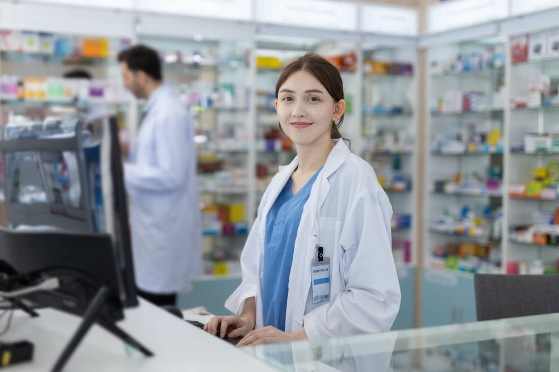 Woman pharmacist at counter with drug shelf store chemical products background. 