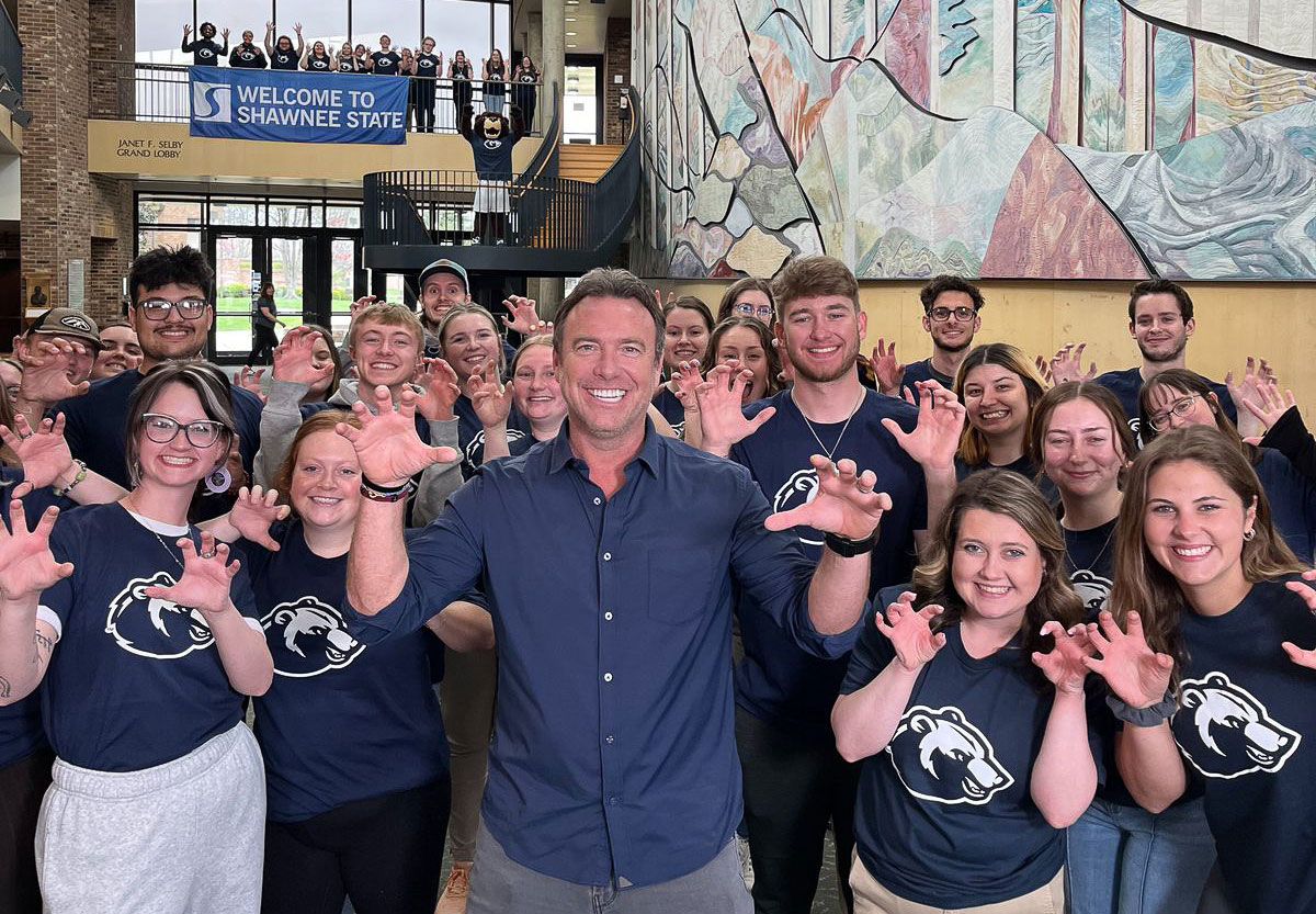 Group of Shawnee State students and a host Alex Boylan posing indoors with "Paws Up" hand gestures.