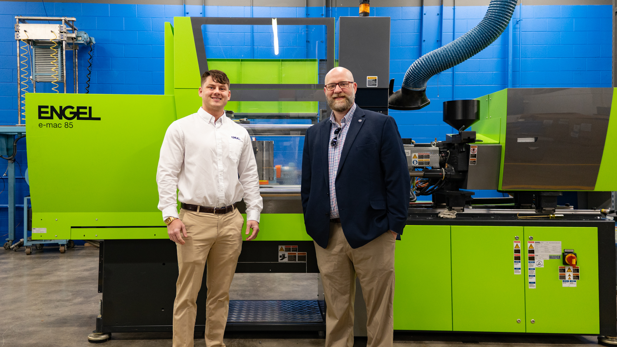 Two men standing in front of a bright green ENGEL injection molding machine in a manufacturing center.