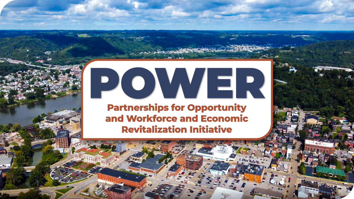 Aerial view of a riverfront city with a banner reading “POWER: Partnerships for Opportunity and Workforce and Economic Revitalization Initiative.”