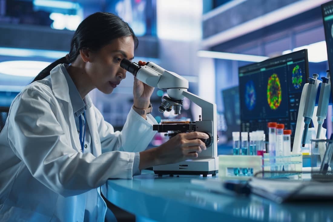 Female Asian Scientist Using Microscope To Analyze Petri Dish Sample.