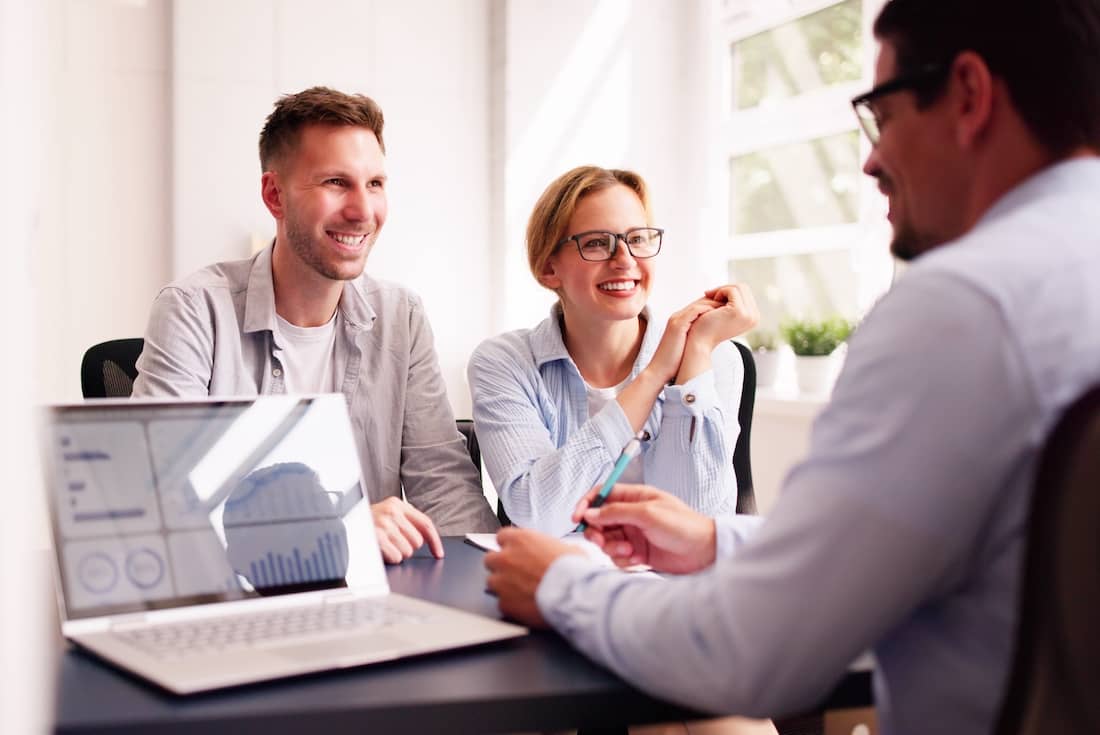 Young couple discussing their financial future with a financial planner in the office using a laptop and notebook.