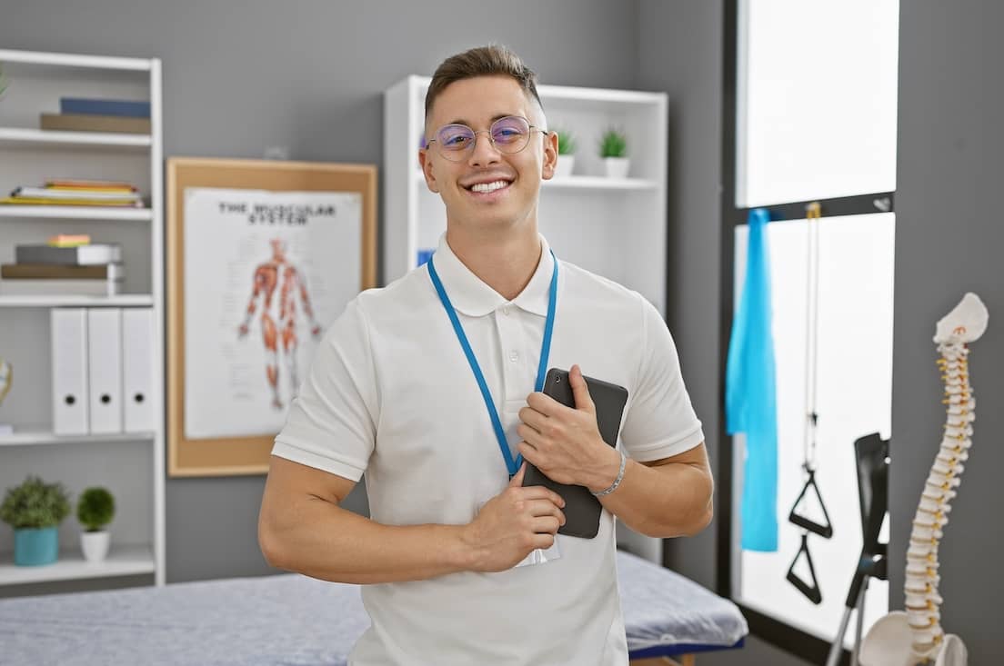 Smiling young hispanic man with glasses, standing confidently in a medical clinic.
