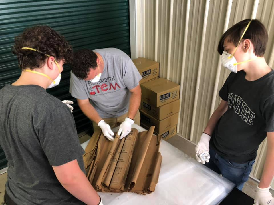three students wearing masks and gloves working with old newspapers