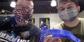 two students in masks holding face shields in plastics lab