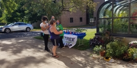 Four people in masks in front of table of trees