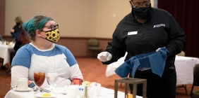 A masked student and server at a dinner table