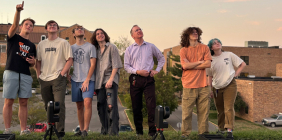 Group of seven people standing outdoors at sunset, looking upward together in front of SSU campus buildings