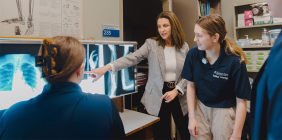 Instructor points to X-ray images while radiologic technology students review scans in a lab.
