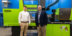 Two men standing in front of a bright green ENGEL injection molding machine in a manufacturing center.