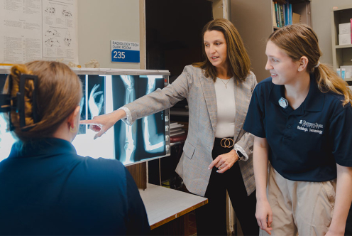 Instructor points to X-ray images while radiologic technology students review scans in a lab.